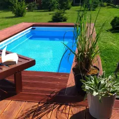 Wkopanie basenu stelażowego w drewniany taras. Na leżaku leży otwarta książka, obok donice z roślinami.