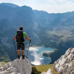 Trekking w Czarnogórze: turysta z plecakiem i kijkami stoi na skale, podziwiając górskie jezioro i pasma górskie.