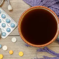 Tasse Kaffee, Stethoskop, Pillen und eine lila Decke. Vielleicht ist es Zeit für die **Selen Einnahme** und einen warmen Kaffee.