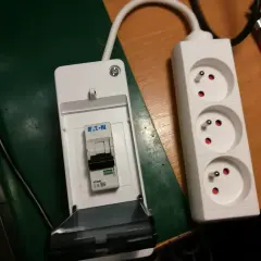 Złączki elektryczne: wyłącznik nadprądowy Eaton w obudowie i biały przedłużacz z trzema gniazdami.