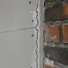 Szczegółowe zbliżenie na łączenie płyt gk z ceglanym murem. Widać nierówności i zaprawę.