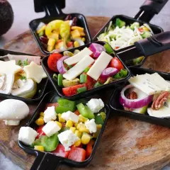 Raclette-Pfännchen mit Käse, Gemüse und Pilzen. Dazu passt ein kühler Weißwein oder ein Bier.
