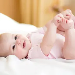 Ein fröhliches Baby von 8 Wochen liegt auf dem Rücken und spielt mit seinen Füßen.