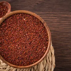 Una ciotola di legno piena di quinoa rossa, con un cucchiaio di legno accanto, su un sottobicchiere intrecciato.