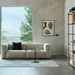 Gemütliches Wohnzimmer mit beigem Sofa, einem Holzsessel und einem Regal voller Bücher. Der Stil ist modern, mit einem Hauch von millennial grey in den Ziegelwänden.