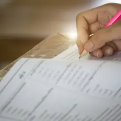 Dłoń ucznia pisząca różowym ołówkiem na arkuszu testowym z kółkami do zaznaczenia odpowiedzi.