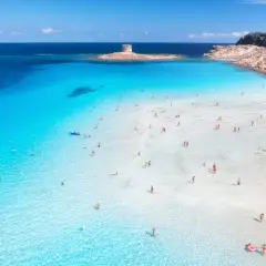 Türkises Wasser und ein alter Turm auf Sardinien. Menschen genießen das flache, klare Meer an einem sonnigen Tag.