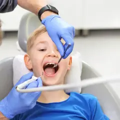 Chłopiec z otwartymi ustami podczas fluoryzacji w szkole. Dentysta w niebieskich rękawiczkach bada ząbki.