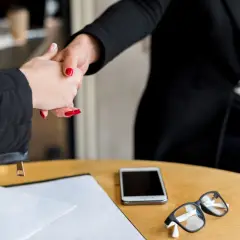 Dwie kobiety ściskają sobie dłonie. Na stole leżą dokumenty, telefon i okulary. Rozmowa o tym, ile kosztuje apelacja w sprawie karnej adwokat.