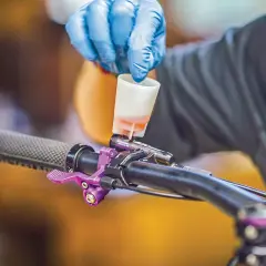 Gloved hand pours fluid into a bike's brake lever, a step in learning how to bleed hydraulic lines.