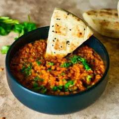 Herzhaftes Linsengericht in einer Schüssel, garniert mit frischer Petersilie und einem Stück Fladenbrot. Perfekt für Linsen Rezepte.