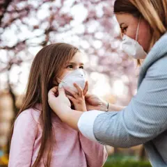 Madre ajusta mascarilla FFP2 a su hija bajo un árbol en flor. Una mascarilla FFP2 para que sirve, protege eficazmente.