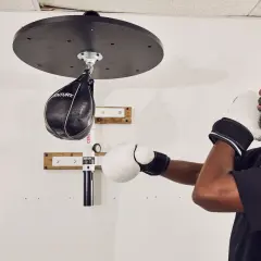 A man in boxing gloves trains with a speed bag, working his shoulder and arm muscles.