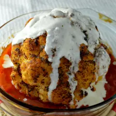 Hel blomkål i ugn, gyllene och kryddad, badar i en smakrik tomatsås och toppas med en krämig sås. En festlig rätt!