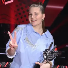 Młoda artystka z pucharem i znakiem pokoju, radośnie świętuje zwycięstwo w The Voice Kids.