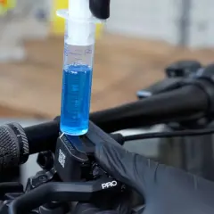 A syringe filled with blue fluid is used to bleed the brakes on a bicycle.