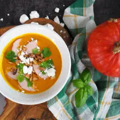 Pomarańczowa zupa dyniowa z mięsem, serem feta, orzeszkami i kolendrą, obok dynia.