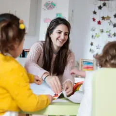 Eine Kinderpflegerin lächelt, während sie mit Kindern bastelt. Sie fragt sich, wie viel verdient man als Kinderpflegerin?