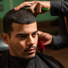 Mann bekommt einen Buzz Cut 15mm. Der Friseur trimmt das Haar mit einer Schere und einem Trimmer.