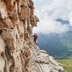 Wspinacz na via ferrata w Dolomitach, z widokiem na kręte drogi i zielone doliny.