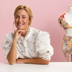 Mujer sonriente junto a un maniquí con un traje colorido de upcycling moda. Montón de pompones de colores a la izquierda.