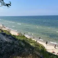 Piękna plaża z wydmami, idealna na orzechowo atrakcje. Woda w morzu jest spokojna, a na piasku widać kilka osób odpoczywających.