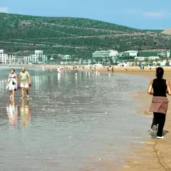Spacerem po plaży w Maroku, w tle białe budynki i zielone wzgórza. Idealne wakacje.