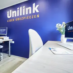 Biuro z niebieską ścianą z logo Unilink, biurkiem, komputerem i krzesłem.