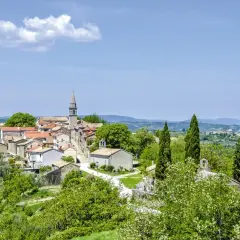 Kleine kroatische Stadt Hum mit Kirchturm, umgeben von grünen Hügeln und Bäumen.