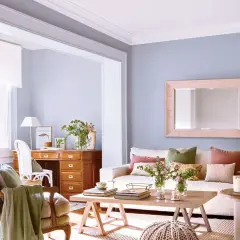 Escritorio de madera con cajonero, silla, sofá con cojines y mesa de centro en una sala de estar luminosa.