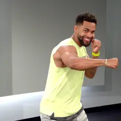 A smiling man in a yellow tank top throws a side hook punch, ready for his next workout move.