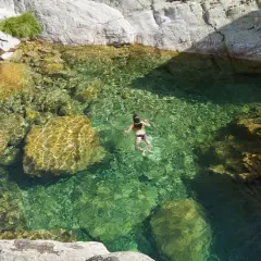 Una persona nada en pozas naturales de agua cristalina en la sierra de Madrid, rodeada de rocas y vegetación.