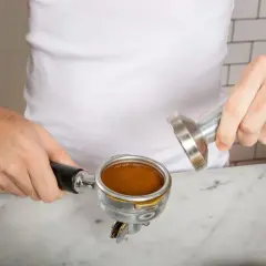Ręce przygotowują kawę cappuccino, ubijając świeżo zmieloną kawę w portafiltrze.