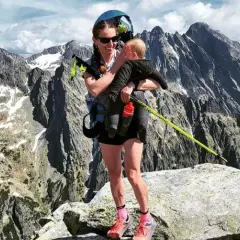 Justyna Kowalczyk z dzieckiem na szczycie górskim, w tle majestatyczne, skaliste pasmo.