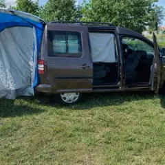 Un caddy tramper aménagé avec une tente latérale bleue et grise, prêt pour l'aventure en plein air.