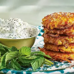En stapel gyllene halloumi morotsbiffar serveras med en krämig yoghurtsås och färsk mynta.