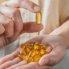 Dłoń trzyma garść kapsułek z olejem rybim, bogatym w kwasy omega 3. Jedna kapsułka jest podniesiona między palcami.