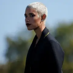 Mujer con **pelo blanco** corto y brillante, maquillaje oscuro y un pendiente llamativo en la oreja.