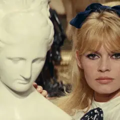 Brigitte Bardot z niebieską kokardką we włosach, obok antycznej rzeźby. Ikona lat 60 muzyka i stylu.