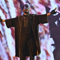 The Weeknd w masce i błyszczącym stroju na koncercie w Polsce, z rękami rozłożonymi szeroko.