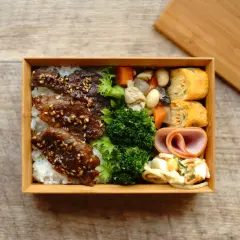 A delicious Japanese convenience store bento box filled with rice, teriyaki beef, broccoli, tamagoyaki, ham, and salad.