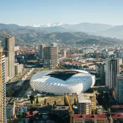 Widok na nowoczesne miasto z futurystycznym stadionem i górami w tle. Rozwój infrastruktury, budowa nowych wieżowców. Batumi ceny nieruchomości mogą być tu atrakcyjne.