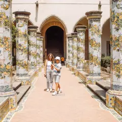 Cortile con colonne decorate a maiolica, un classico del museo Napoli. Una madre e un figlio passeggiano tra gli archi.