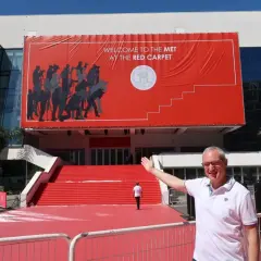 Mężczyzna pozuje przed budynkiem z wielkim czerwonym banerem "Welcome to the Met at the Red Carpet". To przygotowania do festiwalu w Cannes.