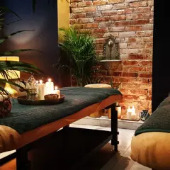 Dwie łóżka do masażu w przytulnym spa, ozdobione świecami i roślinnością.