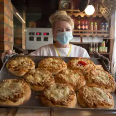Uśmiechnięta sprzedawczyni w maseczce prezentuje tacę z zapiekanymi pizzami. To może być najstarsza pizzeria w Polsce, gdzie tradycja spotyka się z nowoczesnością.