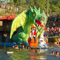 Dragón verde gigante en un desfile acuático, parte de las fiestas de prao Asturias. Gente en el agua y espectadores en la orilla.