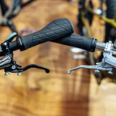 Close-up of bicycle handlebars featuring black Ergon grips and silver and black Hope e4 brakes, ready for any trail.