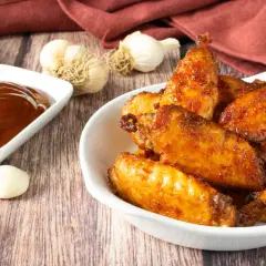 Alette di pollo croccanti e dorate, appena sfornate dalla friggitrice ad aria, servite con salsa barbecue e aglio.