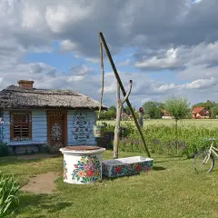 Kolorowy dom malarek w Zalipiu, z kwiecistymi zdobieniami, studnią i rowerem.